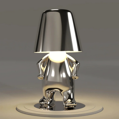 Silver modern figurine table lamp with conical shade over reflective character body, LED-lit