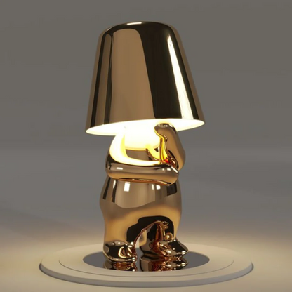 Gold metallic figurine table lamp with glowing conical shade, sculpted body and round base