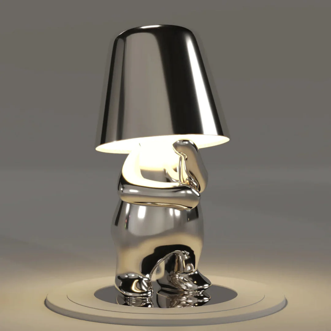 Silver metallic figurine table lamp with glowing conical shade, sculpted body, round base