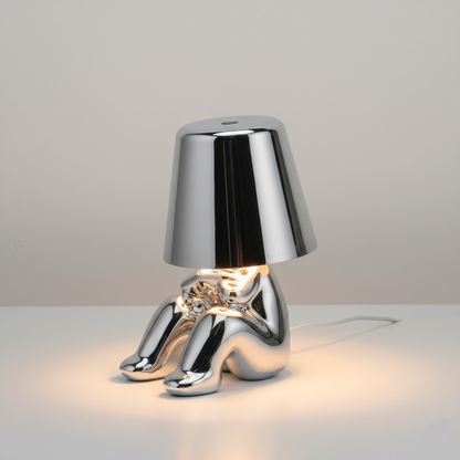 Silver figure table lamp, bell shade with warm light shining onto the base