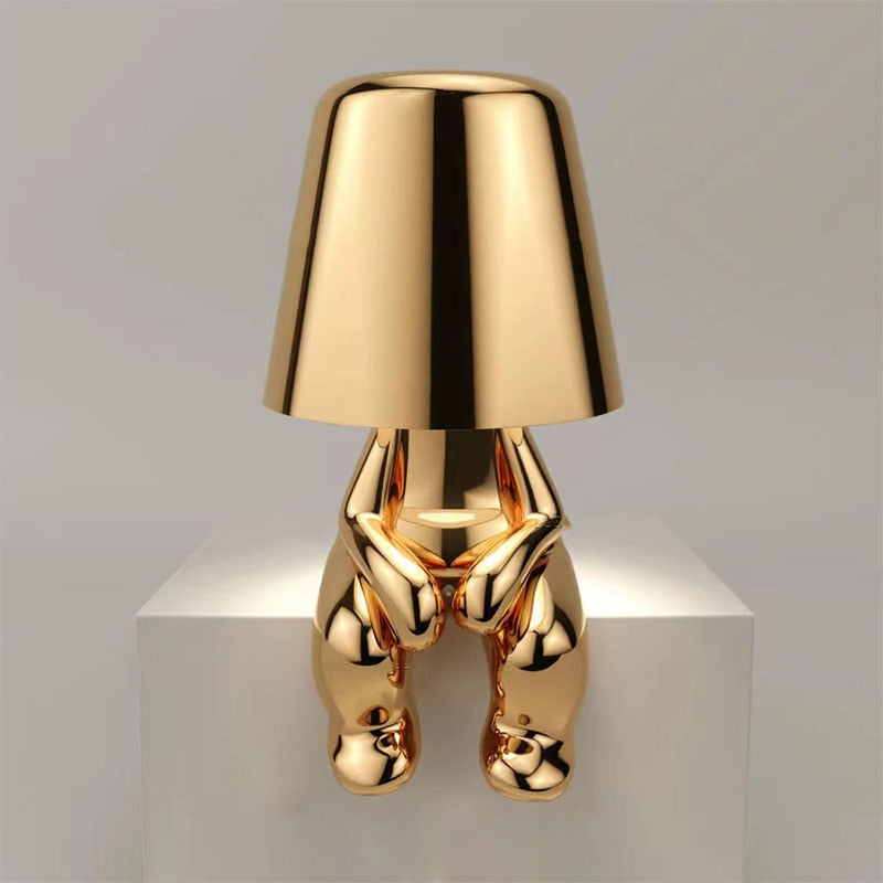 Gold figure table lamp with bell shade and shiny metallic body on a pedestal