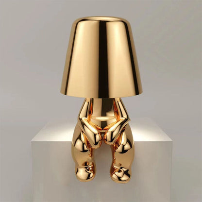 Gold figure table lamp with bell shade and shiny metallic body on a pedestal