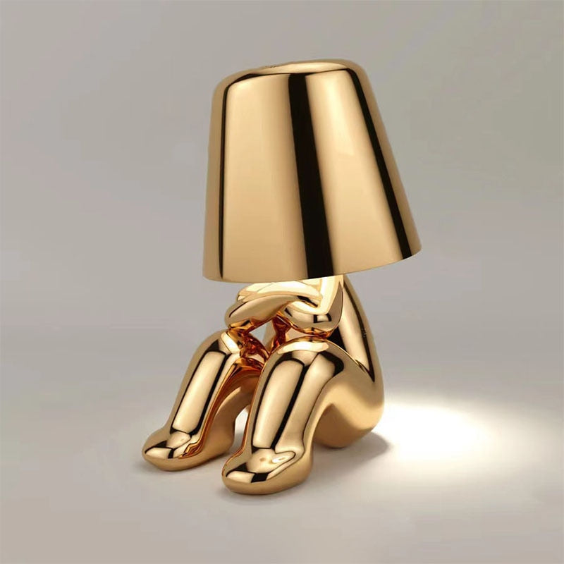 Gold metallic figure table lamp with tapered shade and decorative humanoid base