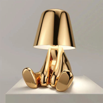 Gold figure table lamp with dome shade and front-facing reflective metallic feet