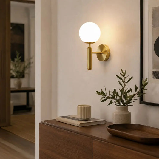 Gold wall sconce with milky glass globe shade mounted on wall above a console