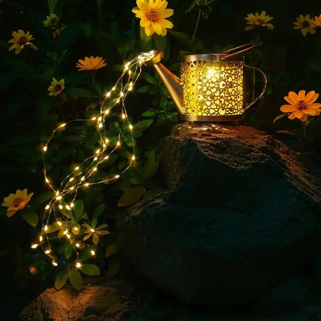 Solar watering can lantern light with warm white fairy string lights over garden stone