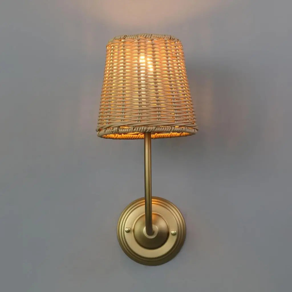 Rattan wall lamp with woven shade and gold wall mount, lit warm glow