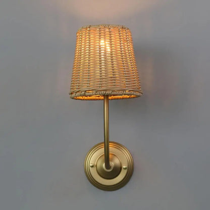 Rattan wall lamp with woven shade and gold wall mount, lit warm glow