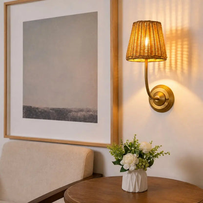 Antique rattan wall lamp with woven shade and gold curved arm, warm glowing bulb