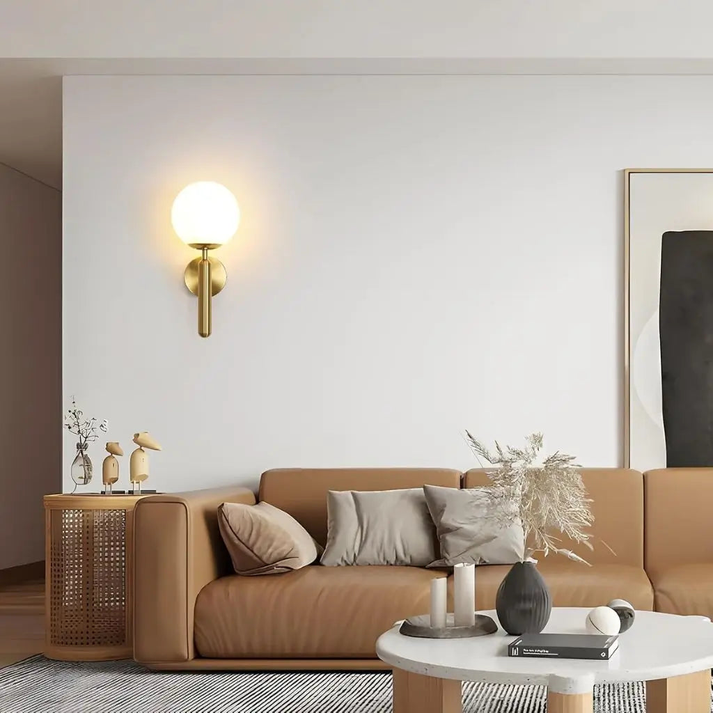 Gold wall sconce with milky glass globe shade and vertical metal arm, switched on