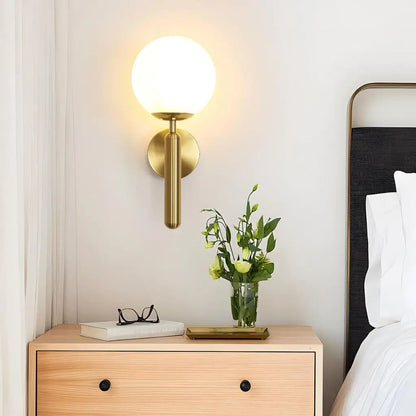 Gold wall sconce with milky glass globe shade mounted beside a bedside table