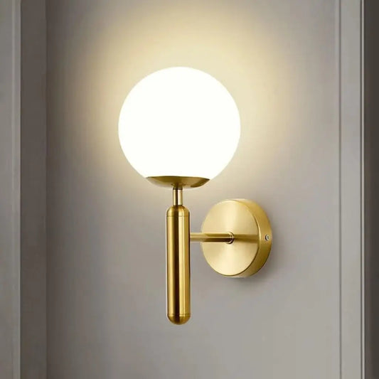 Gold wall sconce close-up with milky glass globe shade and round wall plate