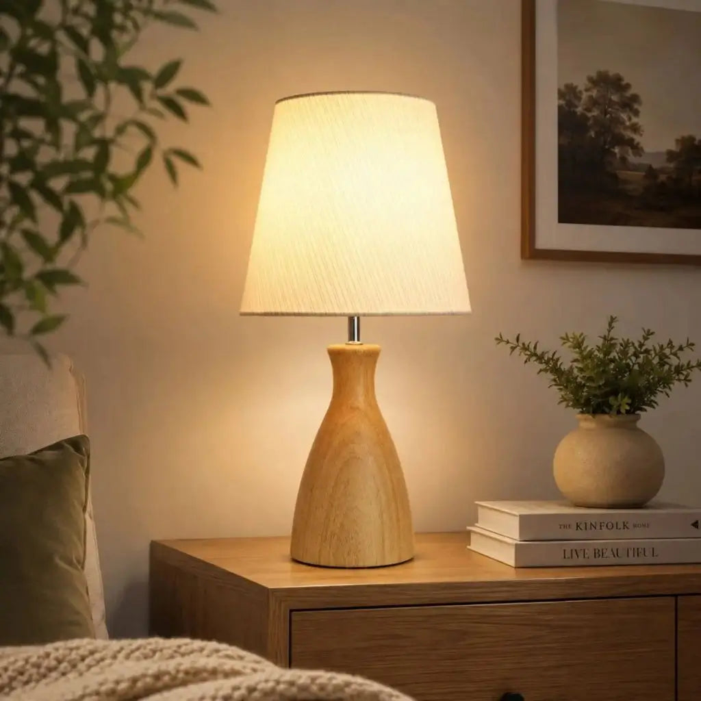 Wooden bedside table lamp with white fabric shade glowing on a side table