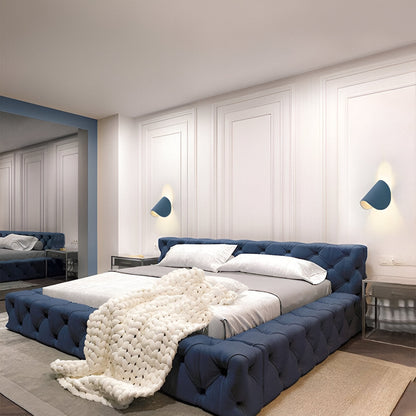 Adjustable metal wall light with dark blue cone shades, mounted above a bed.