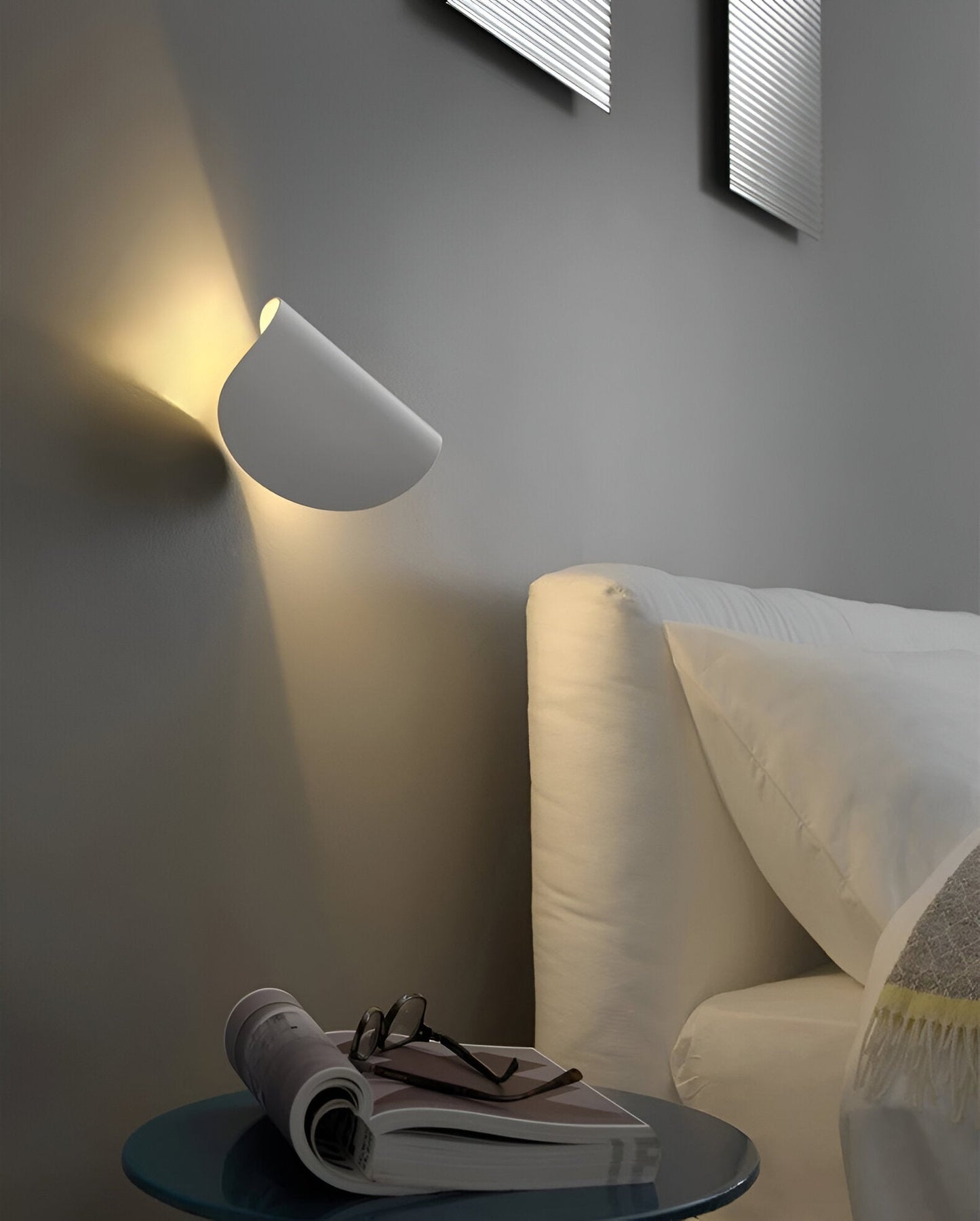 Adjustable metal wall light with light-gray cone shade, casting warm light near wall.