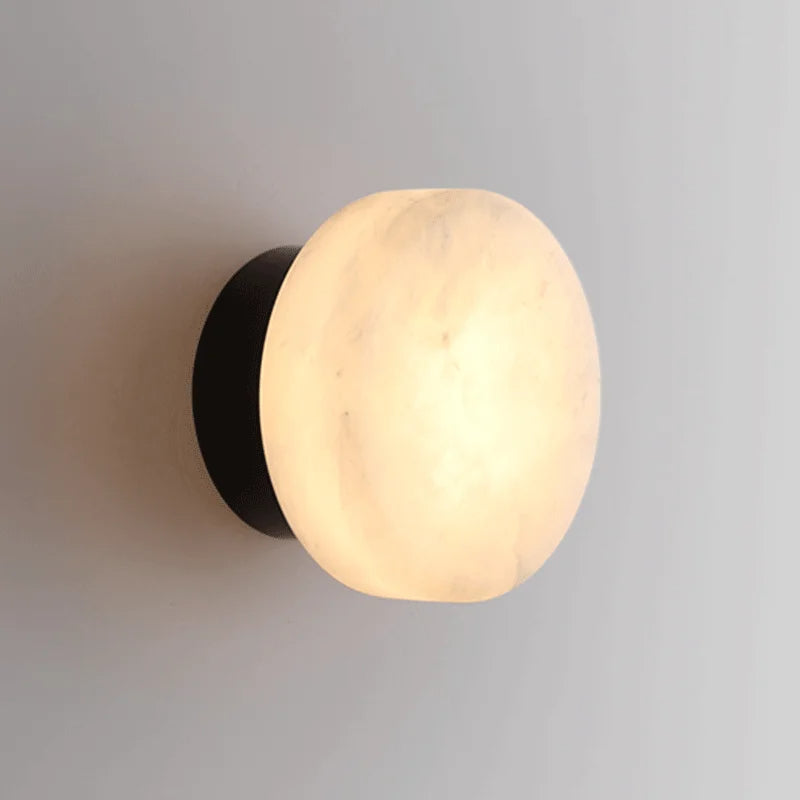 Black LED wall light with round marble-effect diffuser, emitting warm glow