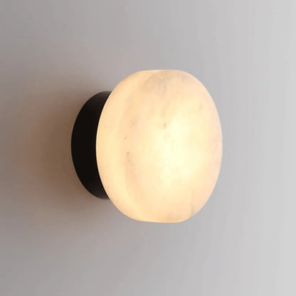 Black LED wall light with round marble-effect diffuser, emitting warm glow