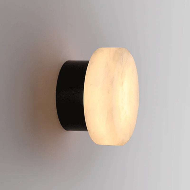 Black-and-marble-effect LED wall sconce with round diffuser emitting warm light