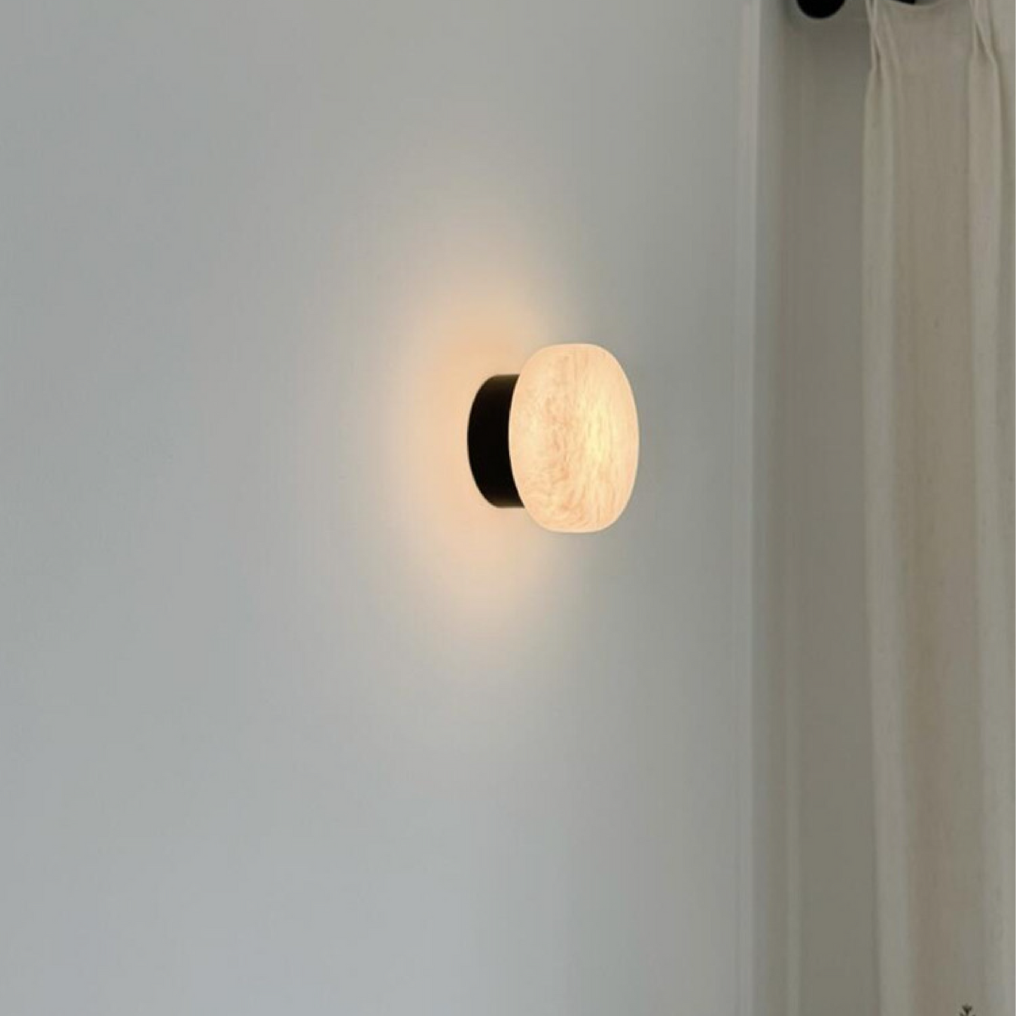 Black LED wall light with round marble-effect diffuser, casting warm ambient glow