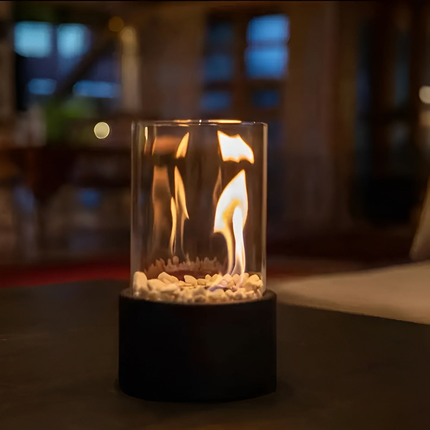 Tabletop bioethanol fireplace with clear glass fire bowl and black metal base, flames inside