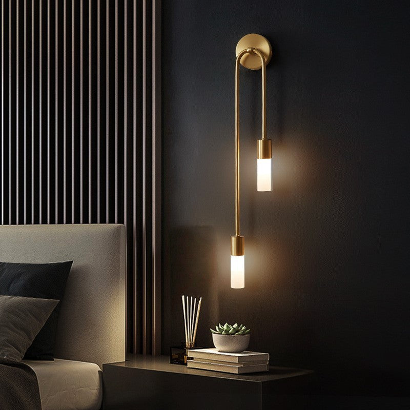 Gold LED wall sconce with curved backplate and two lit warm white cylinder shades