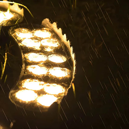 Solar LED garden spotlight shining warm LEDs through rain on a tree trunk