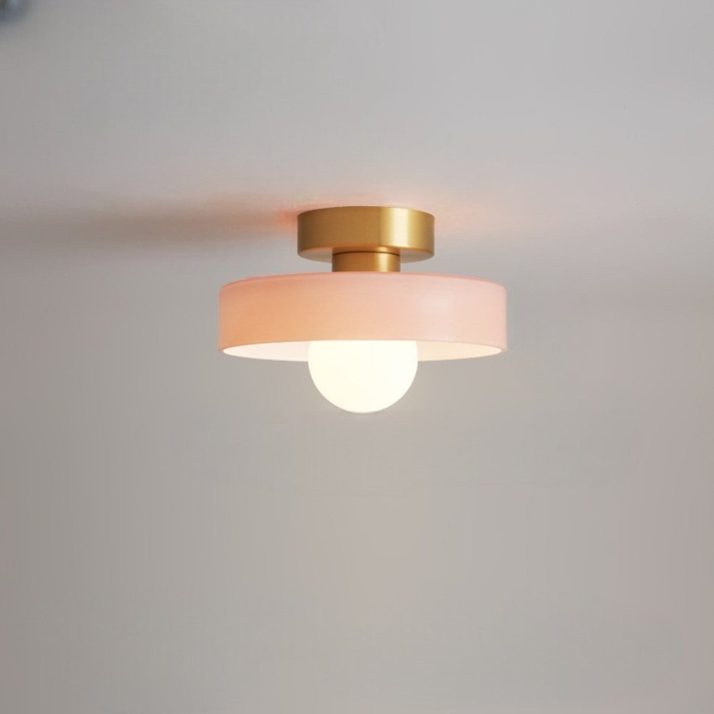 Ceiling light with round peach glass shade and gold metal top, glowing bulb