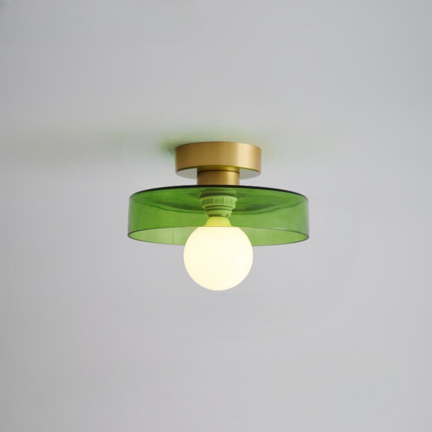 Ceiling light with round green glass shade and gold metal top, glowing bulb
