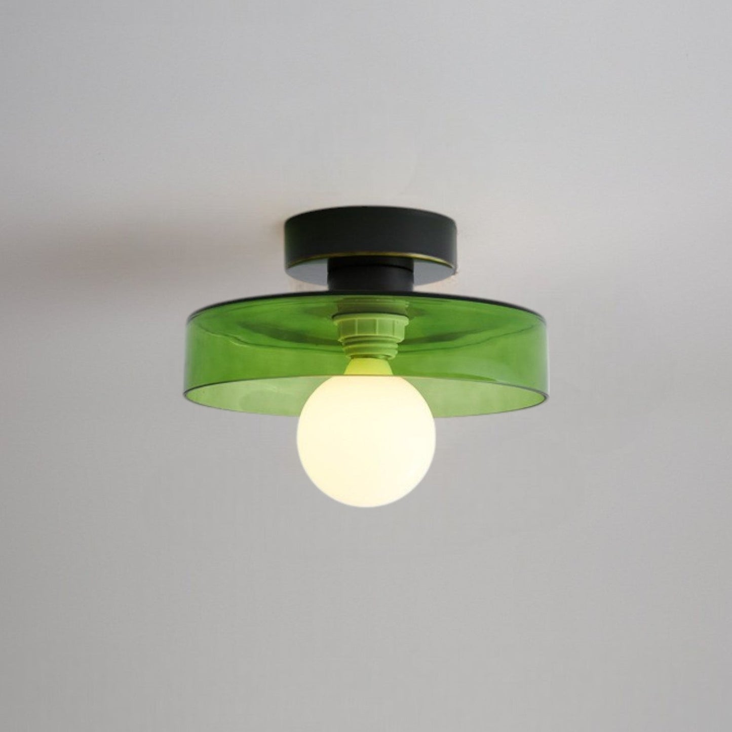 Ceiling light with round green glass shade and dark metal top, glowing bulb