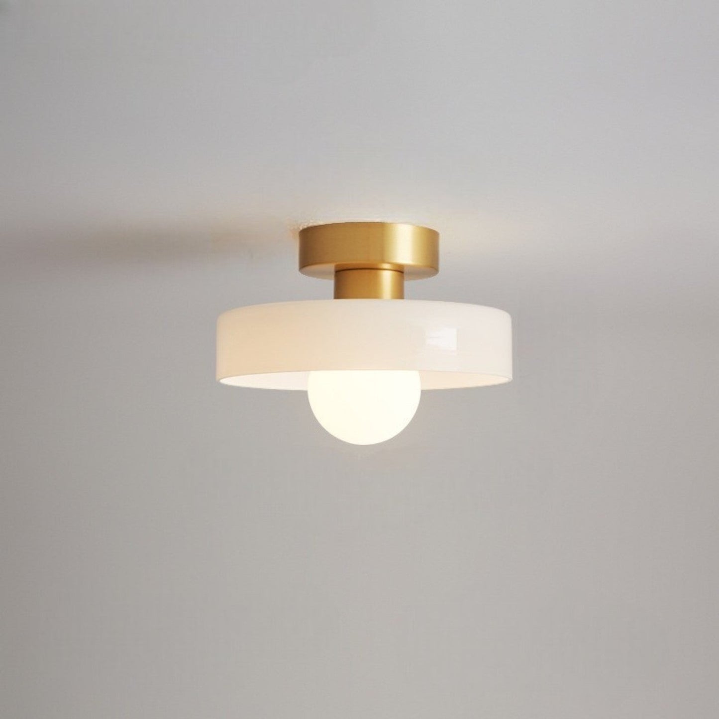 Ceiling light with round white glass shade and gold metal top, glowing bulb