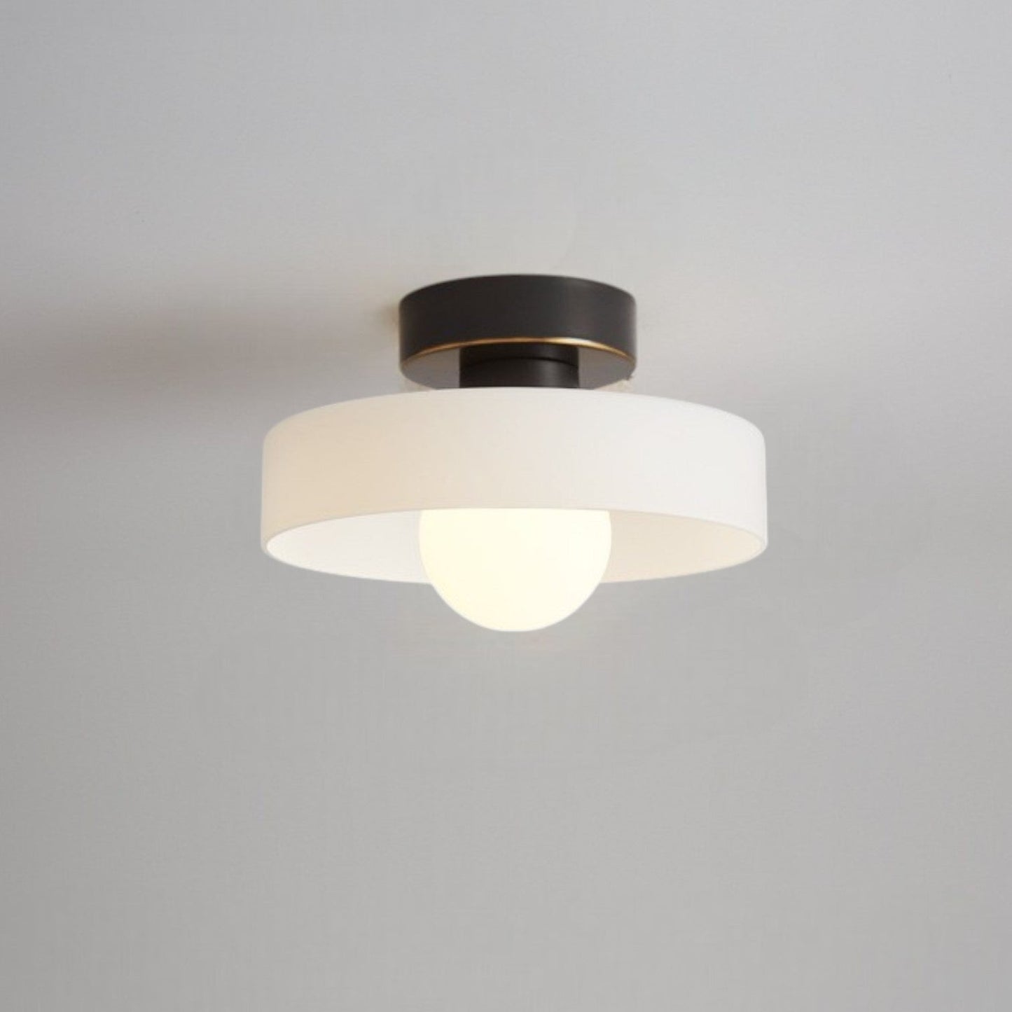 Ceiling light with round white glass shade and dark metal top, with glowing bulb