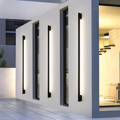 Facade-mounted LED wall light strips with slim dark housings, casting a white linear glow