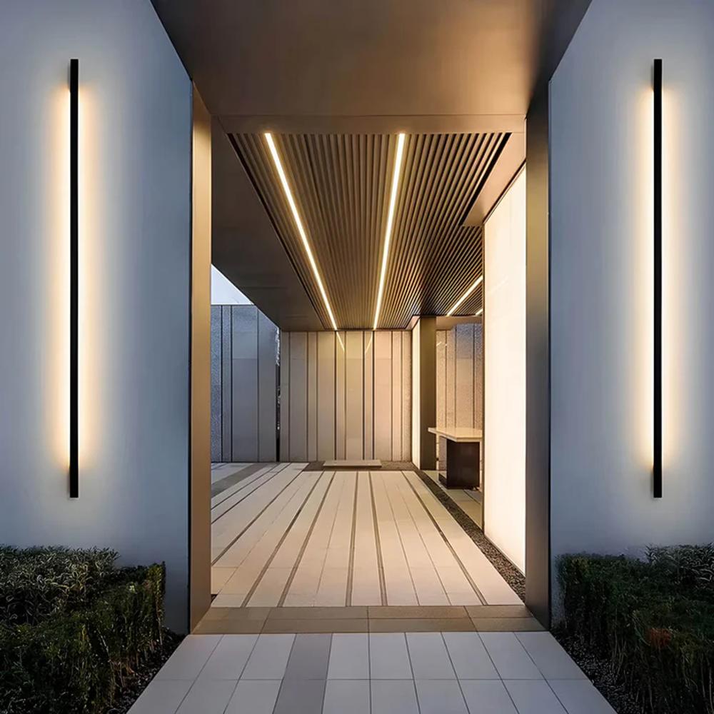 Linear LED wall light strips along a covered walkway, slim dark housings with white glow