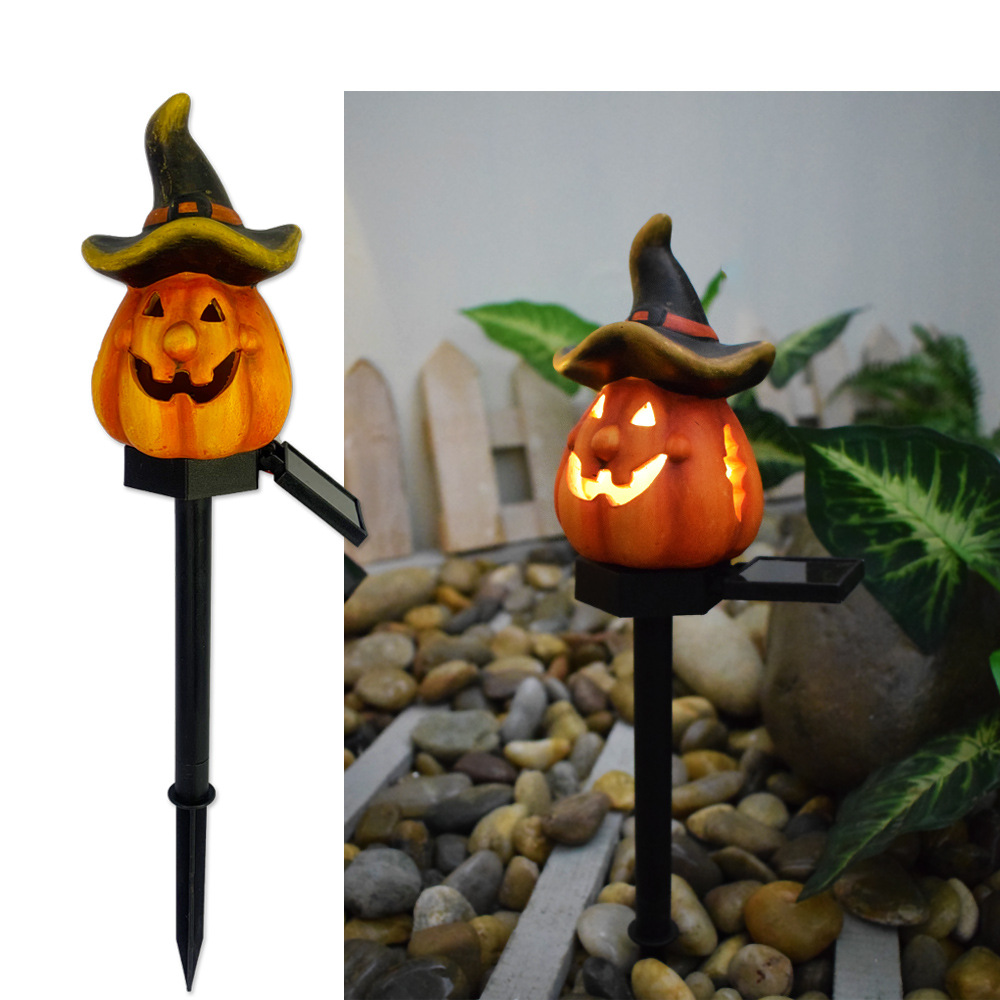 Glowing wizard-hat pumpkin solar garden light on black stake in front of stones