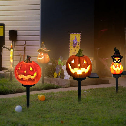 Glowing pumpkin solar garden lights with carved faces on black stakes in yard