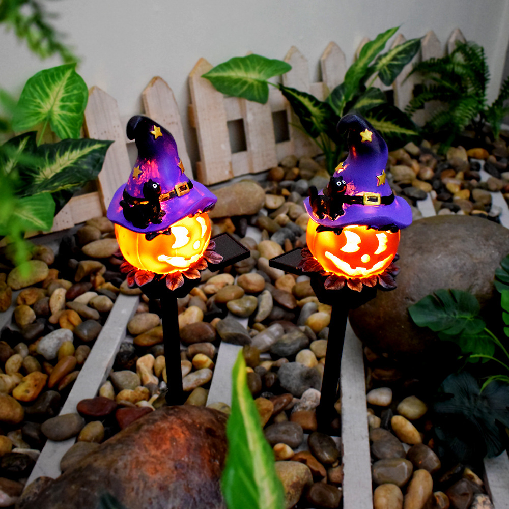 Two glowing witch-hat pumpkin solar lights on black stakes among garden stones and leaves
