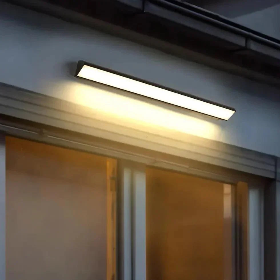Black linear LED outdoor light bar glowing under a roof eave